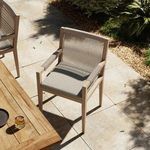 Chair positioned beside outdoor wooden dining table on tiled patio under dappled sunlight