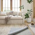 Living room setting showing rug pad under a partially lifted patterned rug near cream sofa