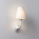 White Winnipeg Wall Sconce with scalloped floral backplate and tapered white linen shade lit softly against pale wall