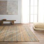 Rug laid flat in a bright, minimalist living room with cushions stacked near large windows