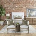 Styled bedroom with bed, rug, two chairs with cushions, side table, brick wall and large plant