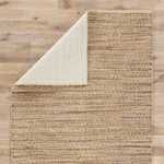 Top-down view showing cotton back of natural tan navy rug with corner partially flipped over