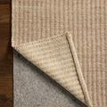 Corner of rug folded to show underside and a grey rug pad beneath on dark wood floor