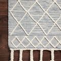 Detailed view of Sawyer Teal Rug patterns with raised, tonal wool diamond shapes and fringe on dark wood floor