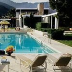 Close view of pool area showing water, concrete patio, lounge chairs, and mid-century modern house facade