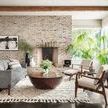 Rustic styled living room with exposed wood beams, brick wall, and Ryan Drum Coffee Table on textured rug near fireplace