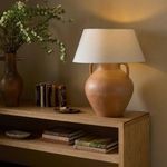 Lamp placed on wooden console table beside books and pottery, lit in ambient room