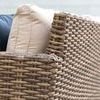 Side close-up highlighting wicker weave and cream cushions with blue decorative pillows