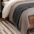 Close-up angled rug under neutral-toned bed linens and rustic wood bench detail.