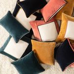 Group of assorted square and lumbar pillows in teal, cream, pink, mustard, and navy velvet scattered on textured rug