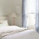 Throw layered at end of bed near window with blue curtains and standing lamp nearby