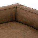 Close-up overview of sofa back and arm showing natural creased leather texture and stitching.