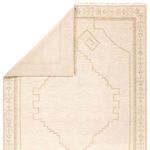 Back corner of rug flipped up revealing tightly woven cream wool backing