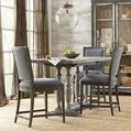 Three Beaumont counter stools styled around a rustic gray wood dining table in a bright room with large windows and a glob...