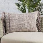 Lumbar pillow styled on light woven outdoor chair with green plant in background