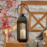 Antoinne Outdoor Lantern placed on wooden chair seat with stone wall and red leaves in background