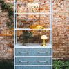 Flynn Etagere styled outdoors against brick wall with flowers, decorative lamp, and yellow hat on shelves