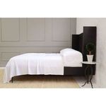 Side angle view showing sheet drape and bed frame legs with textured rug underneath