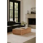 Round Off Coffee Table styled in a living room with black sofa, fireplace, rug, and decorative items on top