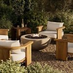 Bronson fire table lit with flames, surrounded by cushioned wooden outdoor chairs and lush green garden setting