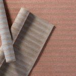Partially rolled rug showing reverse side with lighter taupe and blue stripes