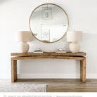 Table styled in a living room with round gold mirror and beige lamps on top