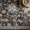 Close-up of charcoal rug corner showing detailed traditional floral and geometric patterns with stacked books and decor