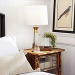 Styling of lamp on bamboo side table next to sofa with beige pillow and white wall paneling