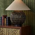 Casimer Black Table Lamp illuminated on wood dresser with patterned green wallpaper and stacked books