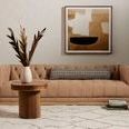 Rug styled under beige tufted sofa and round wood side table with dried plants, neutral decor