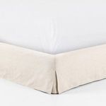 Bedroom setting with queen bed in cream linen slipcover against neutral textured wall