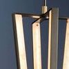 Close-up of illuminated alabaster panels and brass fasteners on Edgemere Pendant with partial frame against dark background