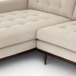 Close-up on corner joint of L-shaped sectional highlighting button tufting and wooden taper legs