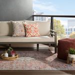 Outdoor patio setting with rug under sofa with beige cushions and patterned pillows