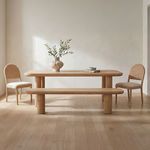 Dining room setting showing bench with two wicker chairs and natural light on wood floors