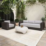 Outdoor arrangement with sofa and armchair on beige rug, stone patio, decorative potted plants, and white rounded coffee t...