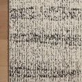 Close-up of rug corner resting on light wood floor showing charcoal linear details and edge