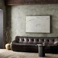Close angle of painting displayed above tufted leather sofa with nearby draped branches in clay pot