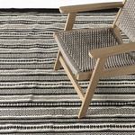 Rolla Outdoor Rug partially under a wooden armchair with woven seat, showing pattern scale and styling context