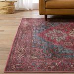 Close-up of rug’s edge under sofa leg showing the worn, vintage-style texture and intricate border