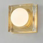 Square wall sconce with soft white illuminated globe and hammered aged brass frame on gray wall