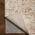 Clarisse rug corner lifted to reveal backside texture and gray rug pad underneath on wooden floor