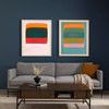 Two framed colorful abstract artworks featuring layered horizontal blocks, hung above a gray sofa in a modern living room