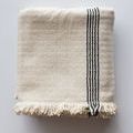 folded cotton throw with black stripe detail and fringed edges on light gray surface
