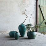 Group of four turquoise jars including the anchor jar styled with plants and dried branch in rustic room setting