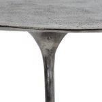 Close-up of oval tabletop edge and slim arm showing textured hammered metal surface in silver