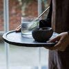 Small Valley Nature Bowl on a round tray with a glass of water and gold straw held by person in apron