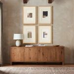 Gallery wall of four mixed media collages above wooden credenza with lamp and decorative objects