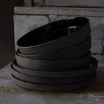 Stack of six Lagoa Eco Gres bowls showing textured exterior and glossy black interiors from an angled side view