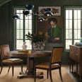 Dining room setting with two Archives Leather Chairs around a round wooden table on a beige rug in a green room with wall art